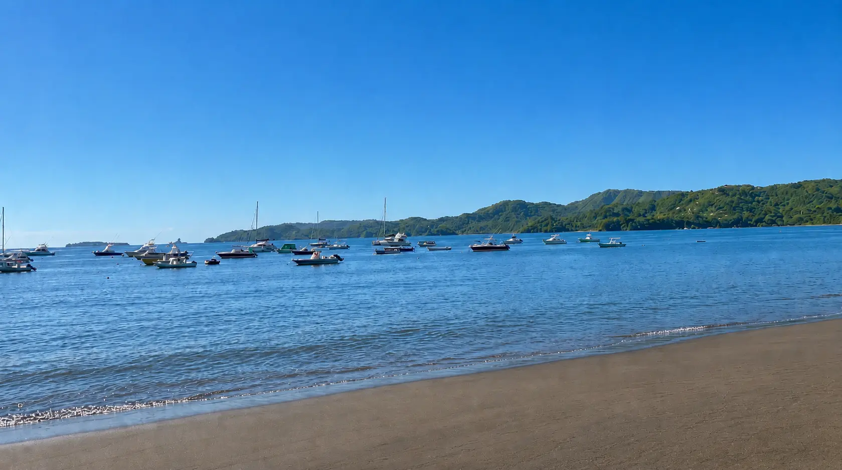 Calm waters of Potrero Bay with fishing boats and sailboats anchored offshore and green hills of Flamingo in the distance