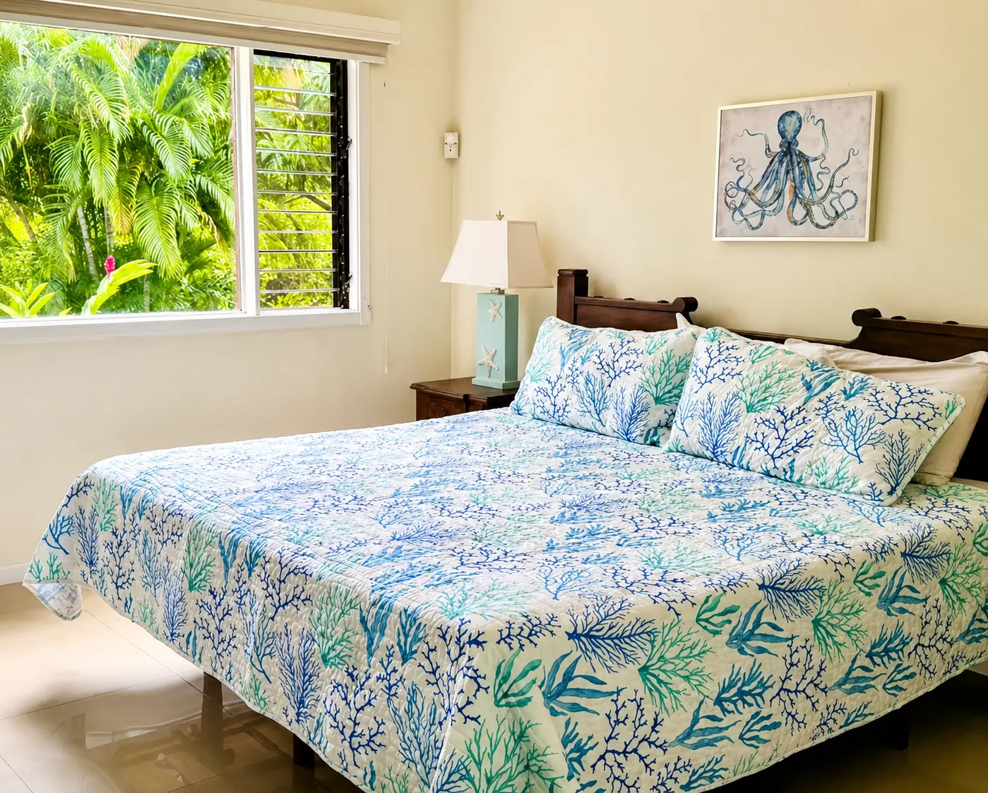 Master bedroom with king bed in coral-print bedding, octopus artwork, and palm trees through the window