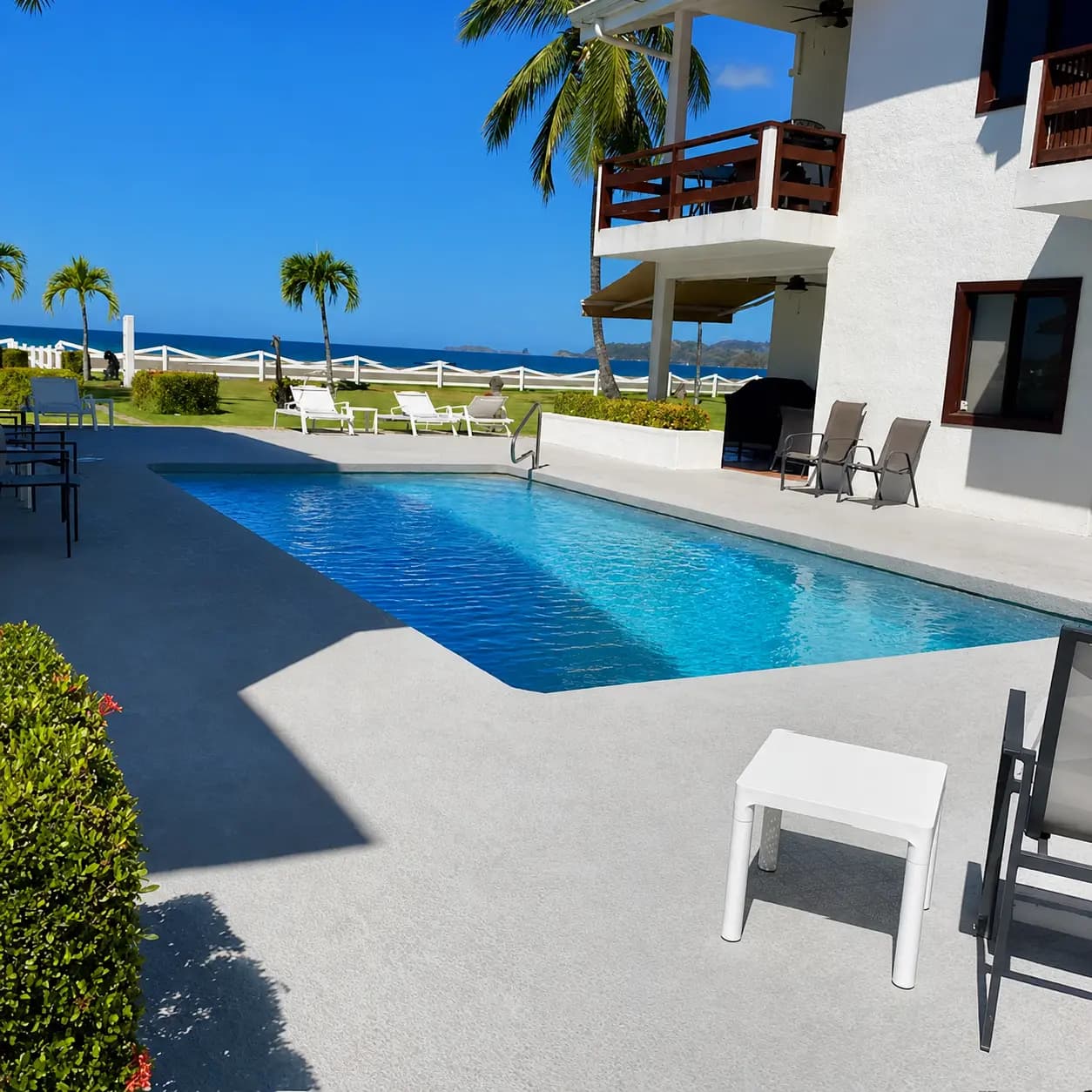 Shared beachfront pool with lounge chairs, palm trees, and the Pacific Ocean just beyond the property grounds