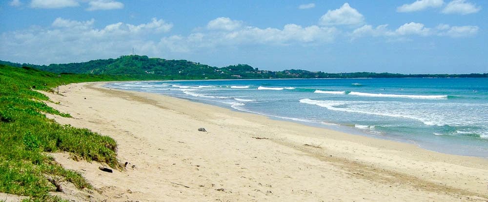 Wide sandy beach at Playa Grande with surf waves rolling in and green hills behind